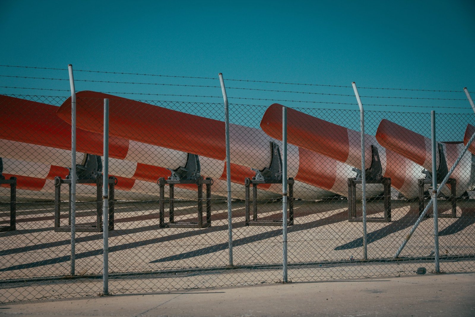 A metal fence with barb wire and metal canoes behind it with blue sky in the background